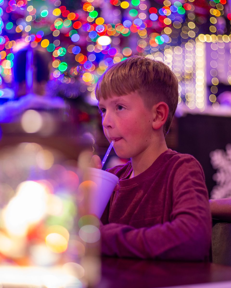 A boy sipping a drink under a canopy of colorful holiday lights